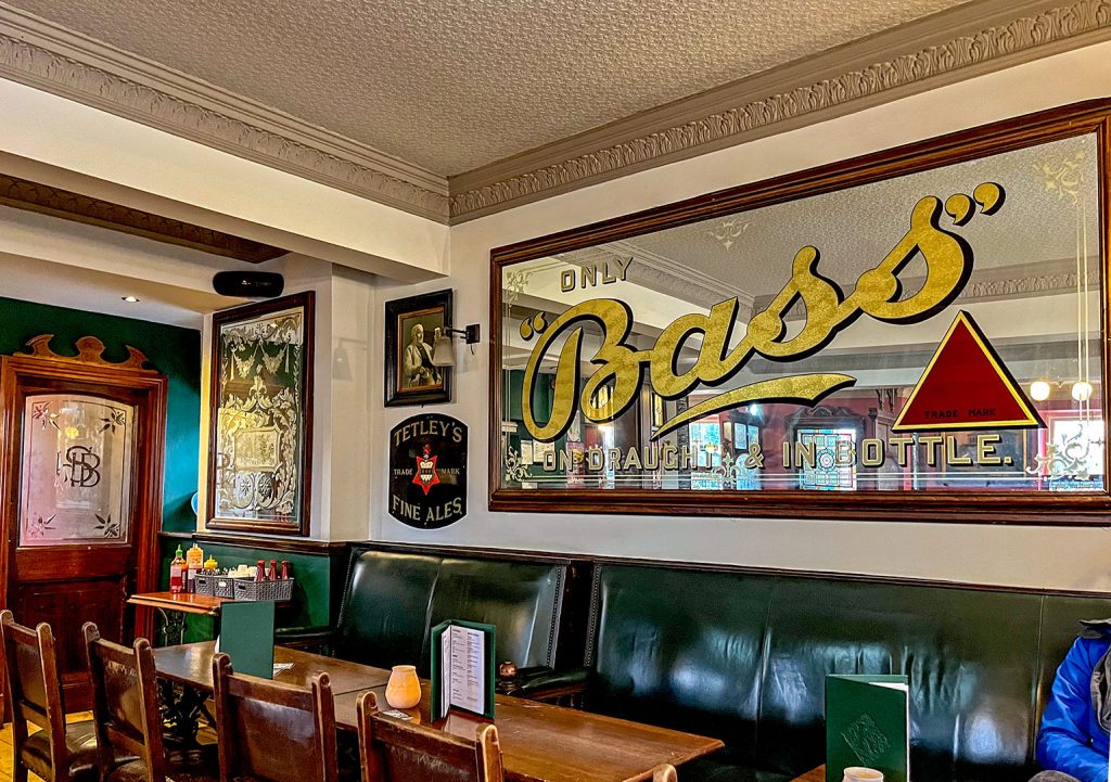 Kirkstall Bridge Inn, Leeds: Large 'Bass' wall mirror and other brewery signs with green upholstered seating.