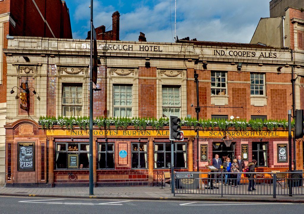 Scarbrough Hotel, Leeds: Brown, yellow and buff tiled exterior with pub name and 'Ind Coope's Burton Ales' signs.