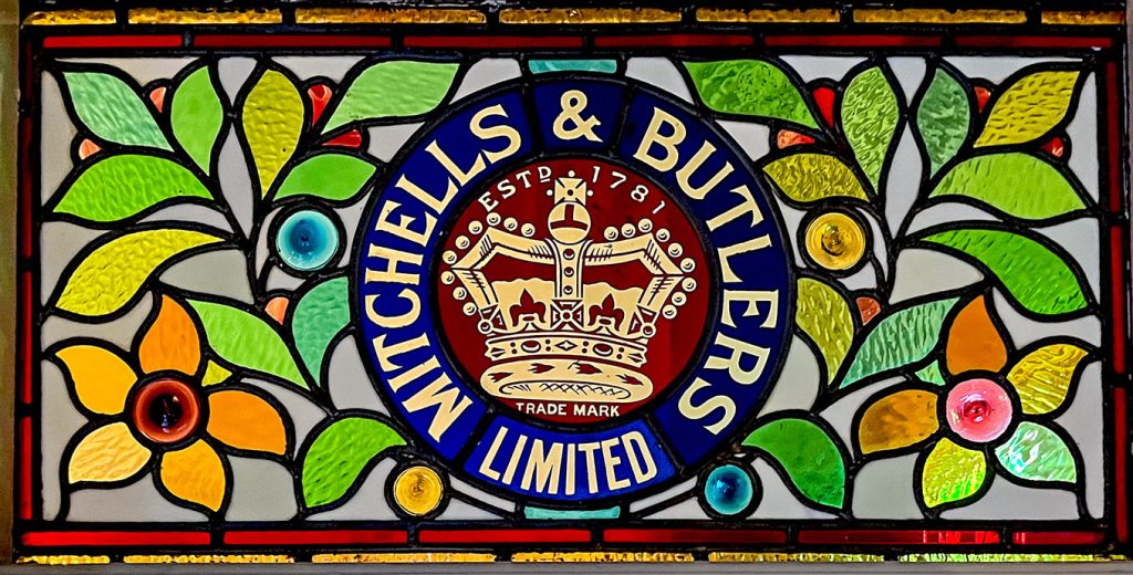 Floral design stained glass window with Mitchell & Butlers Limited logo in the centre