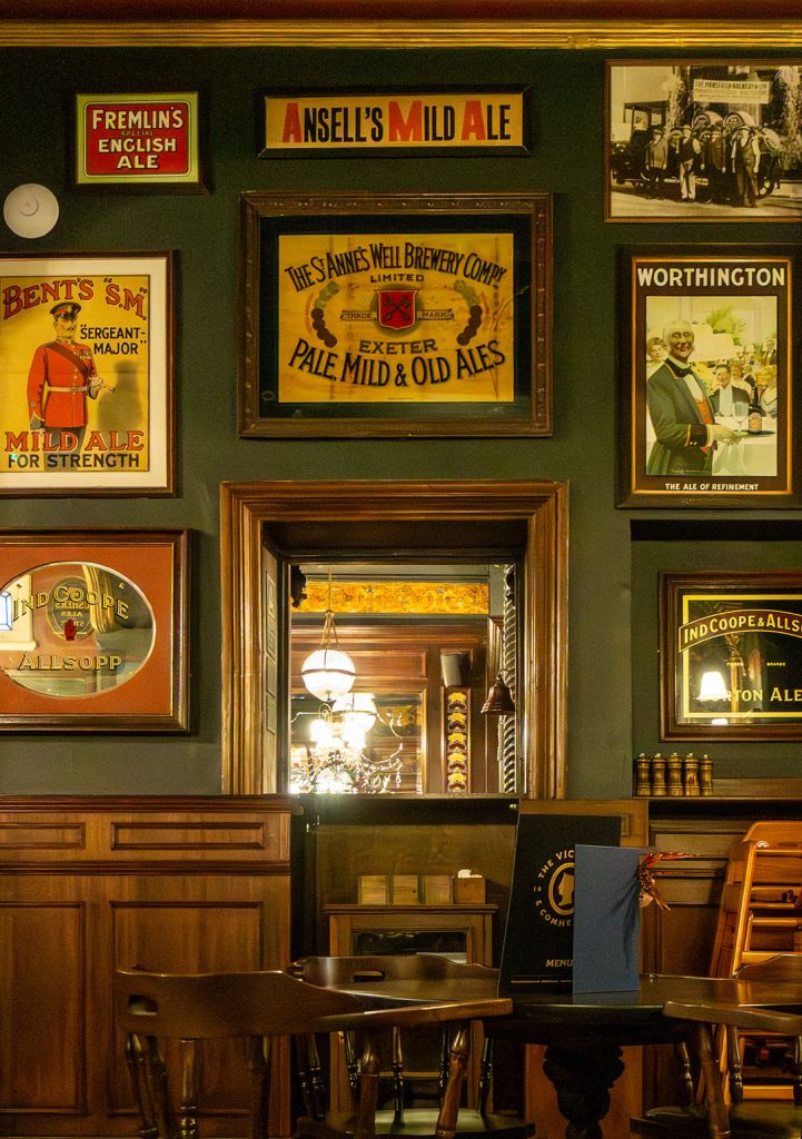 Victoria Hotel, Leeds: Old brewery posters on wall, serving hatch and table and chairs.