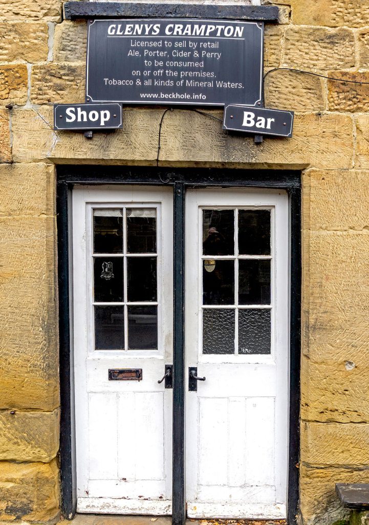 White painted doors to shop on the left and and Small Bar to the right. Liocensing sign above with name of landlady, Glenys Crampton.