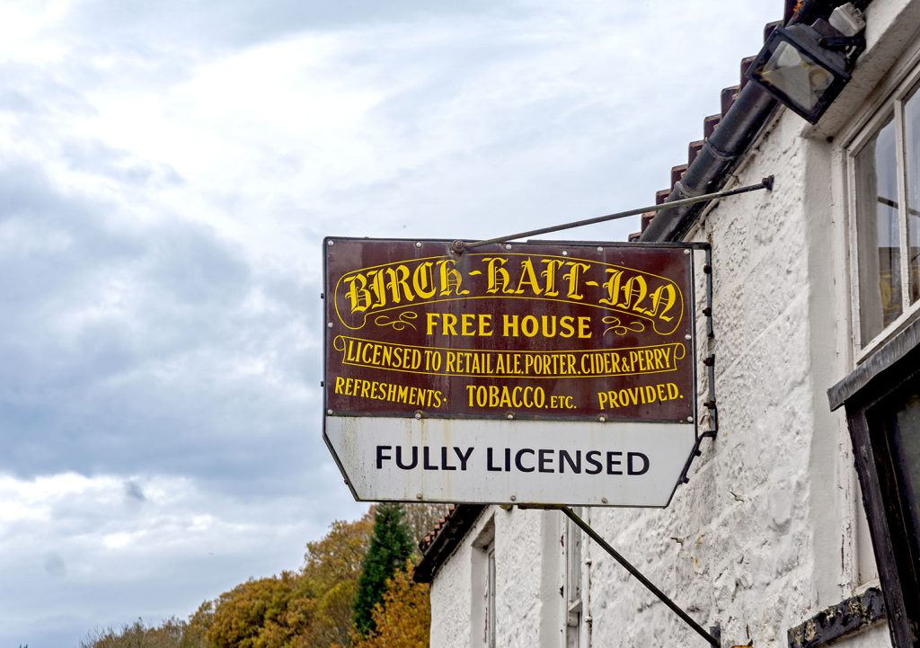 Birch Hall, Beck Hole: The pub's exterior inn sign with pub name and licensing information in yellow on a maroon background.