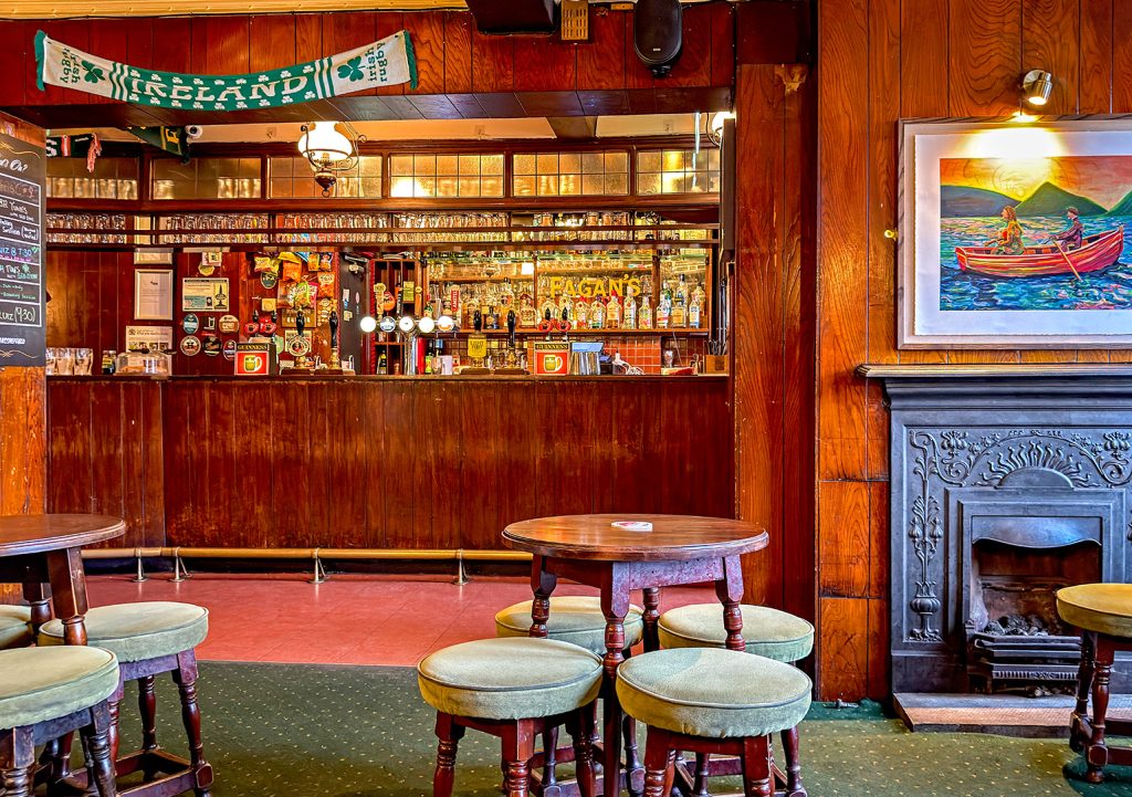 Fagans, Sheffield: View to wood panelled bar counter from main room; black iron fireplace with painting above to right.